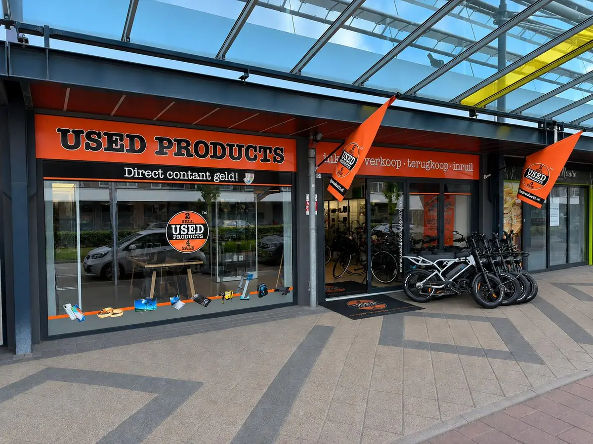 De winkel van Used Products Osdorp aan de Tussenmeer 209 in Amsterdam Osdorp, met oranje gevelreclame en vlaggen onder de overkapping